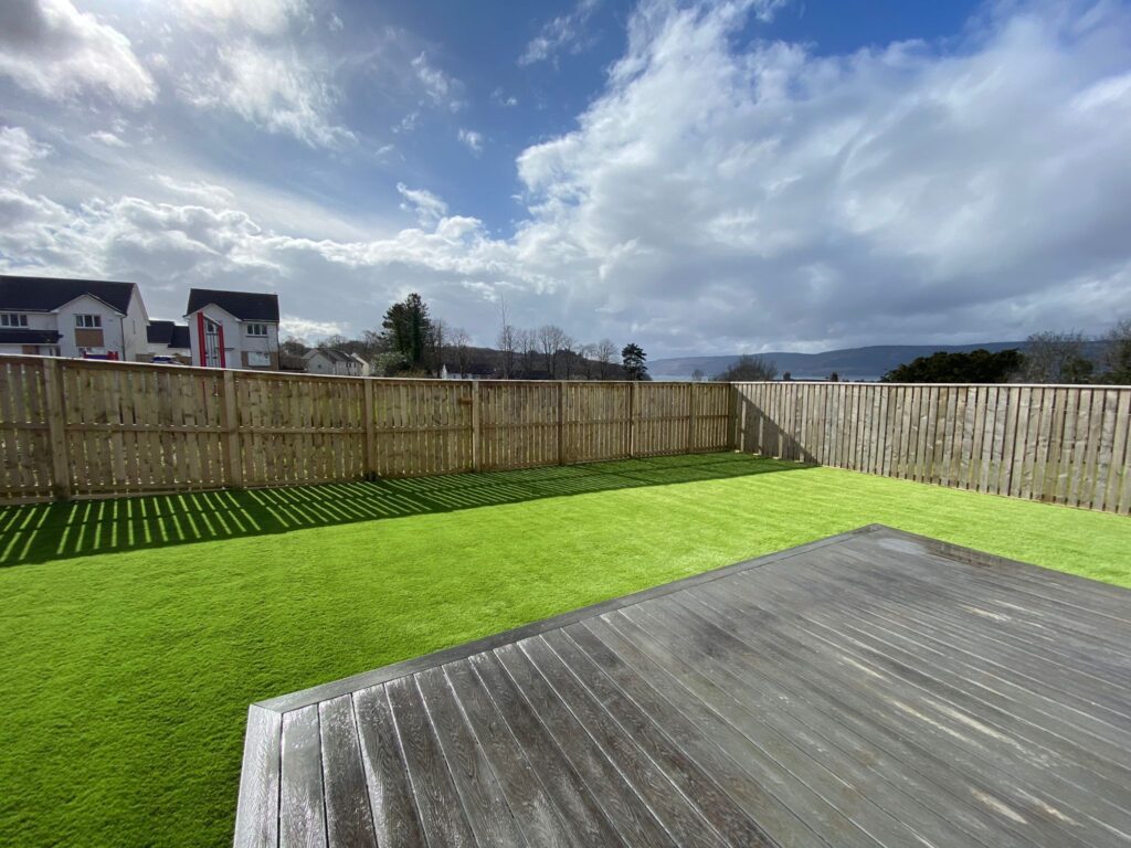 Artificial Grass in back garden of house surrounded by fence.